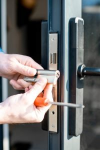 Man changing core of a door lock of the entrance glass door, close-up view with no face